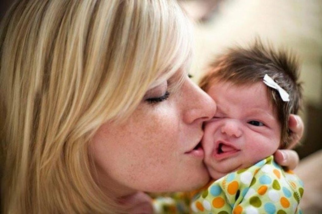 Девушка целует ребёнка, который состроил гримасу. 
