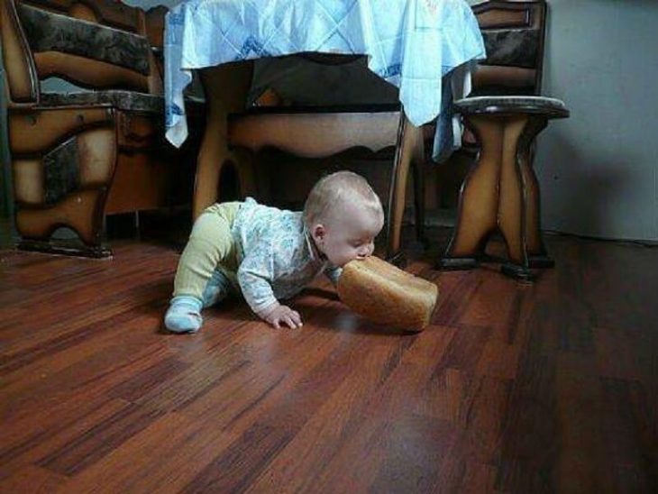 Маленький ребёнок ест на полу целую буханку хлеба.