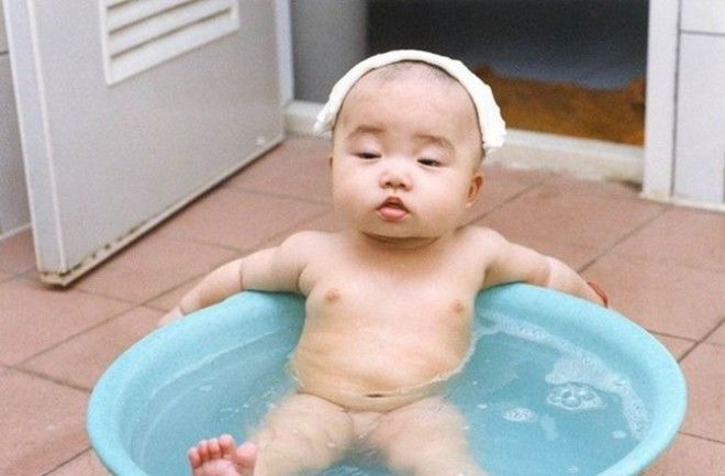 Смешной маленький ребёнок сидит в тазу наполненном водой.