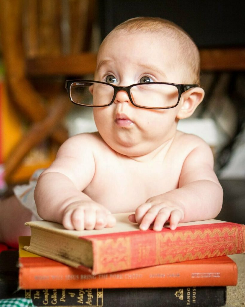 Маленький ребёнок в очках с удивлённым лицом положил руки на книги.