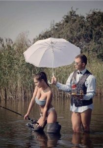 Девушка в купальнике стоит по колена в воде с удочкой, а парень стоит рядом и держит в одной руке зонтик над ней, а в другой поднос с виски и рюмкой.
Рыбацкий юмор, приколы на рыбалке. Фото рыбаков.
