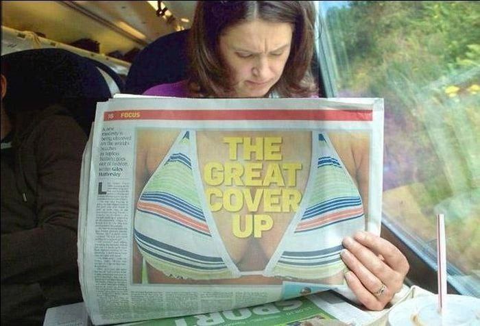 ПОКАЗАЛОСЬ. Девушка в поезде читает газету. Фото в газете - женская грудь в лифчике. Надпись на фото - The great cover up.